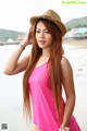 A woman in a pink top and a straw hat on the beach.