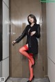 A woman in a black coat and red stockings posing for a picture.