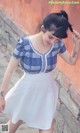 A woman in a blue and white plaid shirt and white skirt.