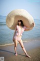 A woman in a pink bikini and a straw hat on the beach.