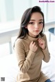 a woman sitting on top of a bed wearing a tan turtle neck top