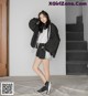 A woman standing in front of a door wearing a black jacket and shorts.