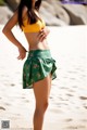 A woman in a yellow top and green skirt on the beach.