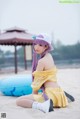 A woman with purple hair sitting on a beach.