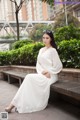 A woman in a white dress sitting on a bench.