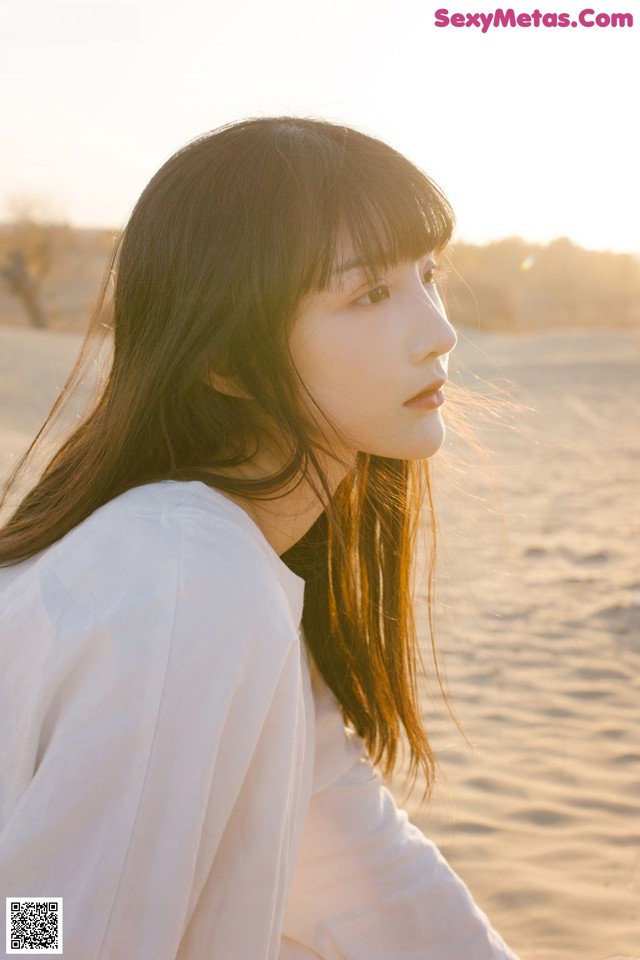 A woman sitting on top of a sandy beach.