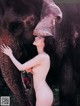 A naked woman standing next to an elephant.