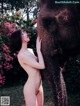 A naked woman standing next to an elephant in a field.