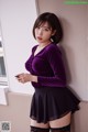 A woman in a purple shirt and black skirt leaning against a wall.