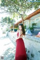 A woman in a red dress leaning against a wall.