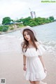 A woman in a white dress and hat standing on a beach.