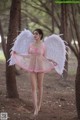 A woman in a pink dress with white wings in the woods.