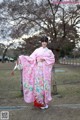 A woman in a pink kimono standing in front of a tree.