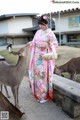 A woman in a pink kimono standing next to a deer.