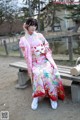 A woman in a pink kimono sitting on a bench.