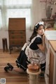 A woman in a maid outfit sitting on the floor in a kitchen.