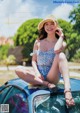 A woman sitting on top of a blue car wearing a hat.