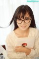 A woman wearing glasses holding a book in front of a piano.