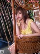 A woman in a yellow dress sitting in a wicker chair.