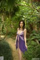 A woman in a purple dress standing in the woods.