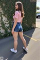 A woman in a pink shirt and blue shorts is walking down the street.