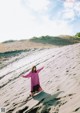 A woman in a purple dress standing on top of a sand dune.