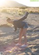 A woman standing in the sand with her arms outstretched.